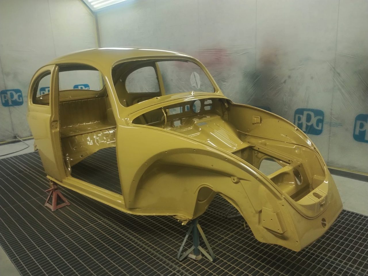 Carroceria de Fusca recém-pintada em amarelo, dentro da cabine de pintura