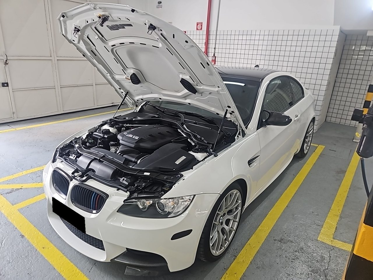 Carro branco com o capô aberto e o motor à vista, dentro da oficina